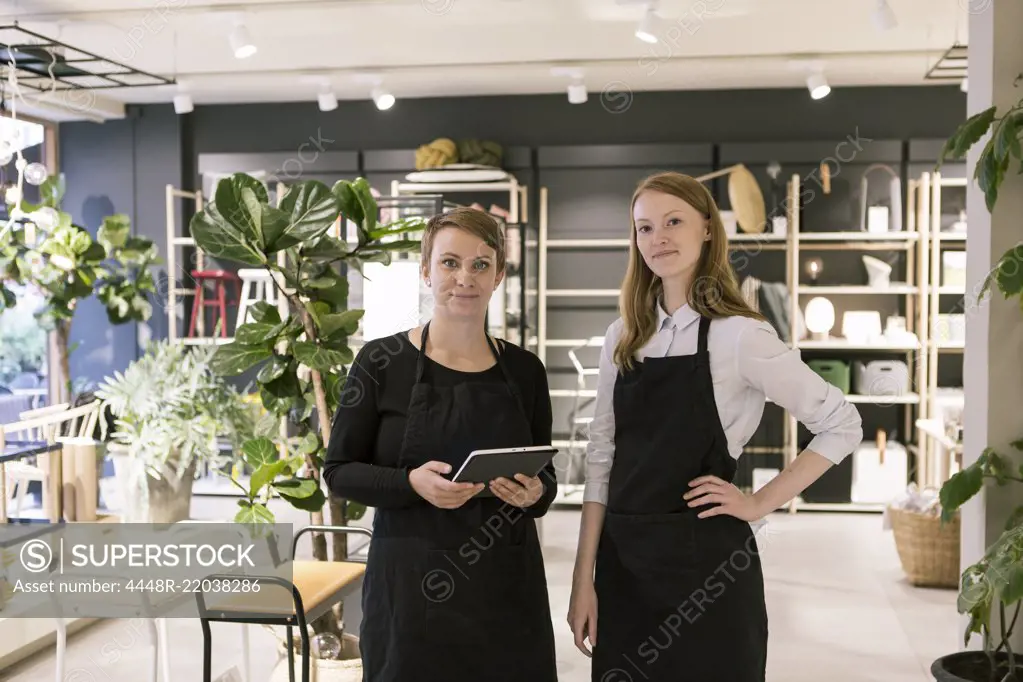 Portrait of owner holding digital tablet while standing with confident partner at store
