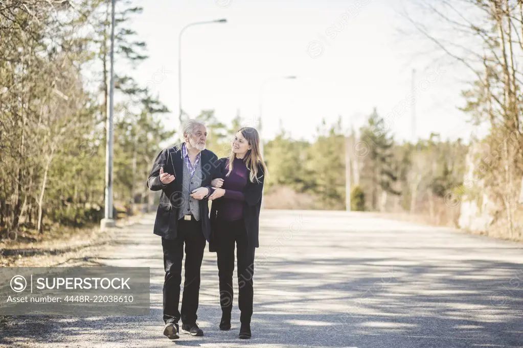 Full length of young woman walking arm in arm with grandfather on road