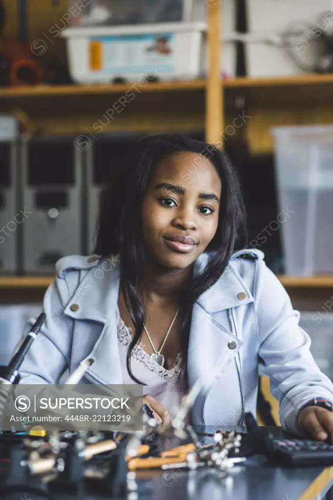 Portrait of smiling female high school student sitting with science project at desk in classroom