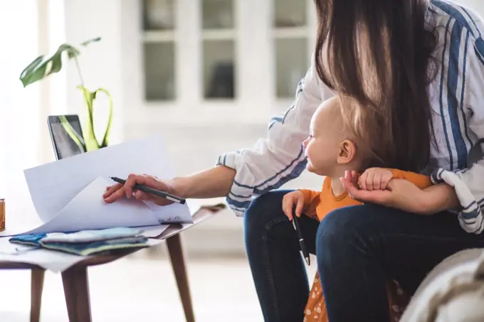 Midsection of working mother examining documents with baby girl at home office