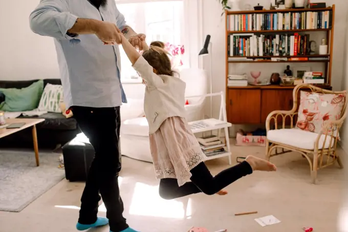 Father swinging playful girl while standing in living room at home