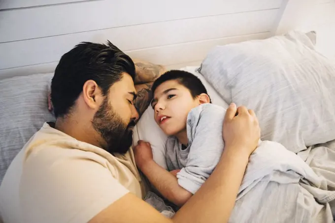 High angle view of father with disable son lying on bed at home