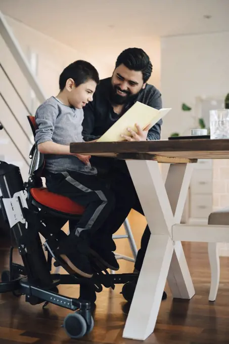 Father teaching autistic son while sitting at table in living room