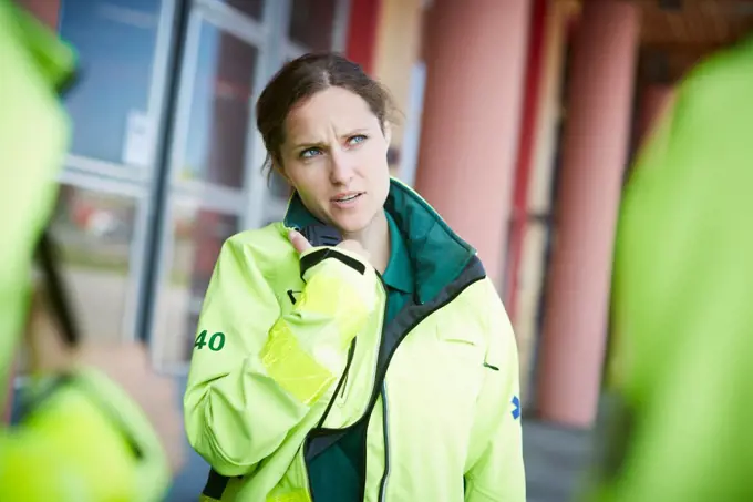 Female paramedic looking away while talking on walkie-talkie outside hospital