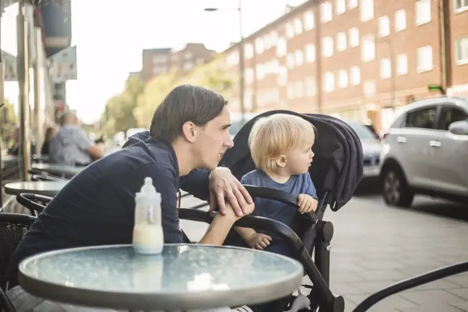 Father and son looking away while sitting at sidewalk cafe in city