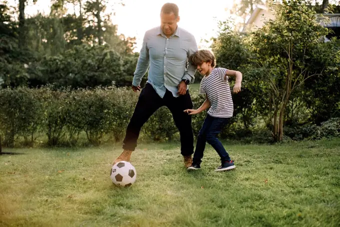 Full length of father and son playing soccer in backyard during weekend activities