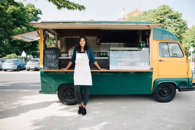 Portrait of smiling female owner standing against food truck