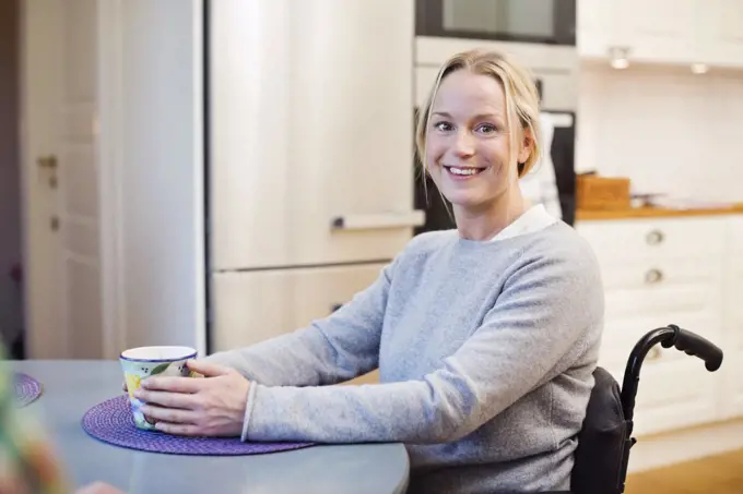 Portrait of happy disabled woman with coffee cup sitting at kitchen