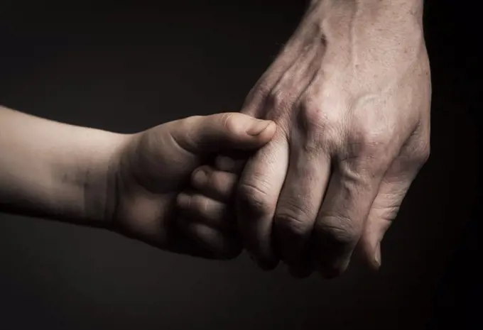 Cropped image of father and son holding hands against black background
