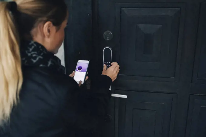 Rear view of teenage girl using smart phone to unlock house door