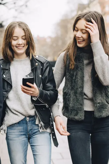 Happy female friends looking at mobile phone in city