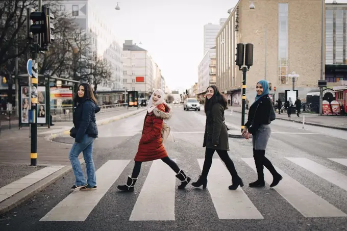 Full length of happy female friends crossing street in city