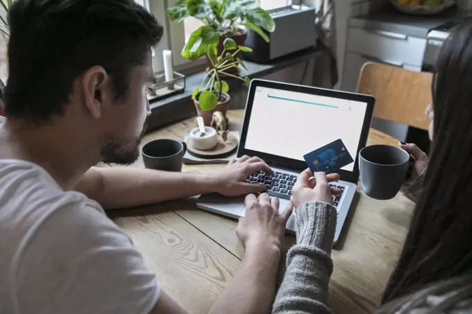 Couple having coffee and using credit card while shopping online through laptop at home
