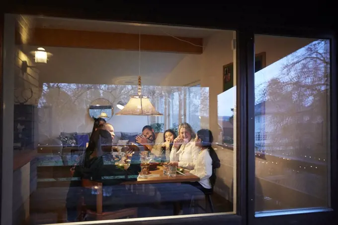 Happy family having dinner at table seen through glass window during sunset