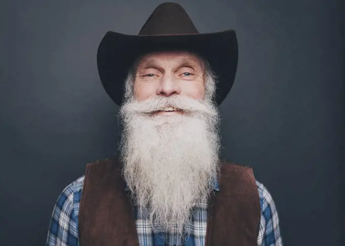 Portrait of happy bearded senior man wearing cowboy hat on gray background