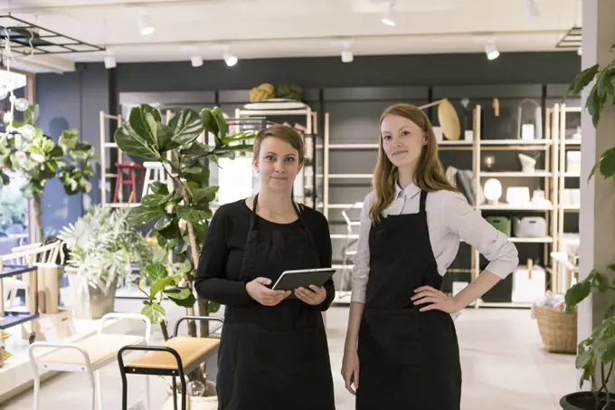 Portrait of owner holding digital tablet while standing with confident partner at store