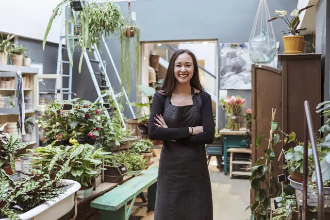 Portrait of smiling female owner standing with arms crossed by potted plants at store
