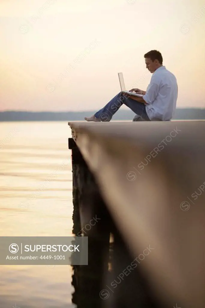 Man using a laptop while sitting on a jetty at lake Starnberg, Ambach, Bavaria, Germany