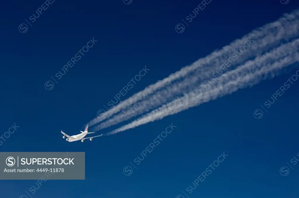 Aircraft with contrails in front of a dark blue sky
