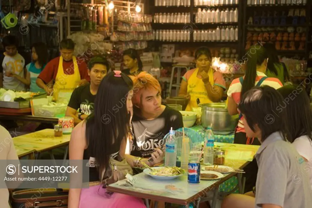 Group of young people sitting at a food stall and eating a snack, Suan Chatuchak Weekend Market, Bangkok, Thailand
