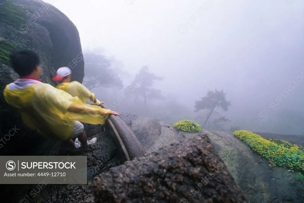 tourists in rain capes descend slippery mountain steps, Huang Shan, Anhui province, fog, stone steps, moss, World Heritage, UNESCO, China, Asia