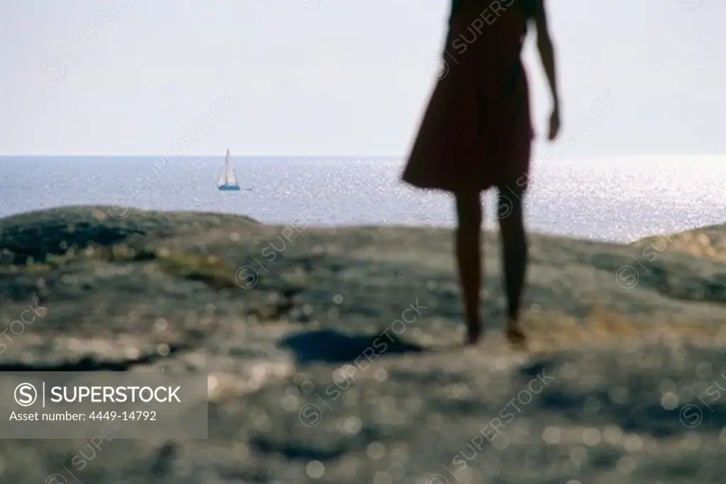 Woman standing on granite rock looking out on sea, Smoegen, Bohuslan, Sweden