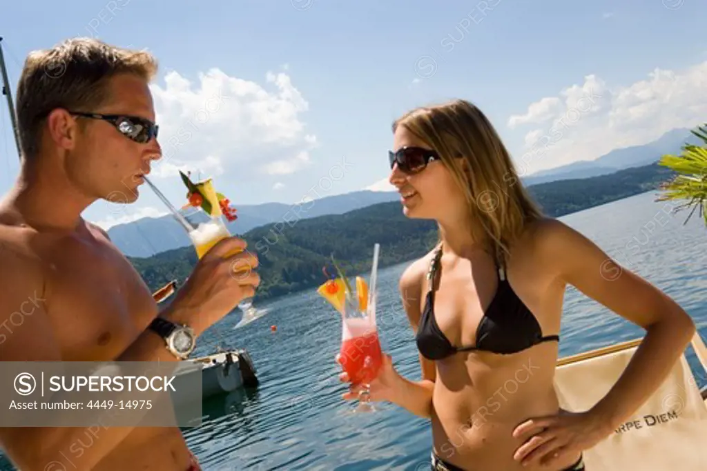 Couple wearing swimsuit and sunglasses drinking fruit cocktails, Millstaetter See (deepest lake of Carinthia), Millstatt, Carinthia, Austria