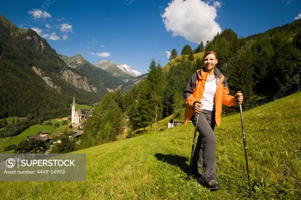 Woman hiking over alp above Heiligenblut with pilgrimage church Zum hl. Pluet, view to Grossglockner, Heiligenblut, Carinthia, Austria