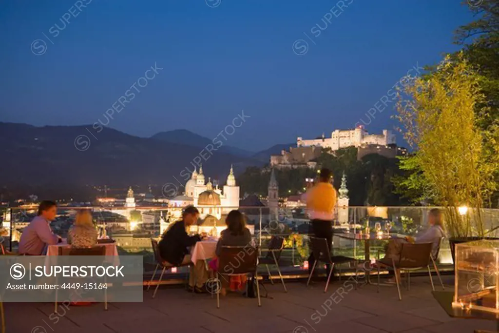 People sitting on terrace of the restaurant Moenchsberg 32 in the evening, view over old town with Hohensalzburg Fortress, Salzburg, Salzburg, Austria, Since 1996 historic centre of the city part of the UNESCO World Heritage Site