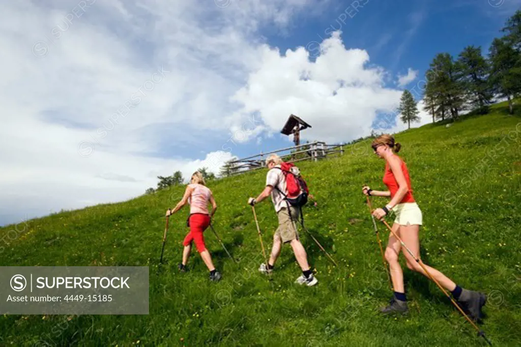 Three hikers walking over a meadow, crucifix above, Grossarl Valley, Salzburg, Austria