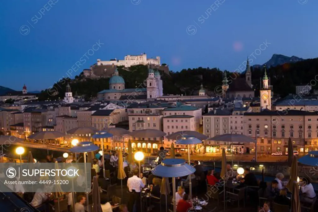 View over illuminated roof deck of restaurant Hotel Stein to old town with Salzburg Cathedral, St. Peter's Archabbey, Franciscan Church, City Hall Tower and Hohensalzburg Fortress, largest, fully-preserved fortress in central Europe, in the evening, Salzburg, Salzburg, Austria, Since 1996 historic centre of the city part of the UNESCO World Heritage Site