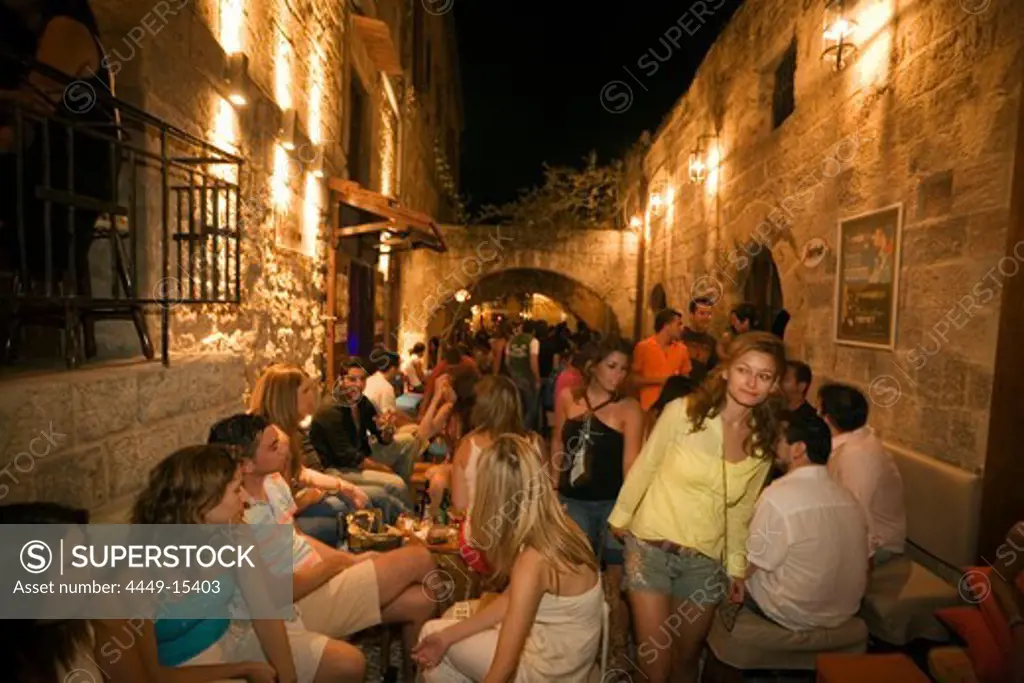 People sitting in outdoor areas of several bars of old town, Rhodes Town, Rhodes, Greece, (Since 1988 part of the UNESCO World Heritage Site)