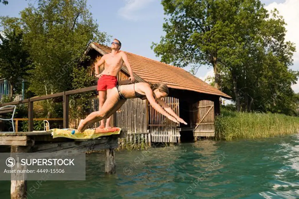 Young woman jumping form a landing stage into Lake Faak, Carinthia, Austria