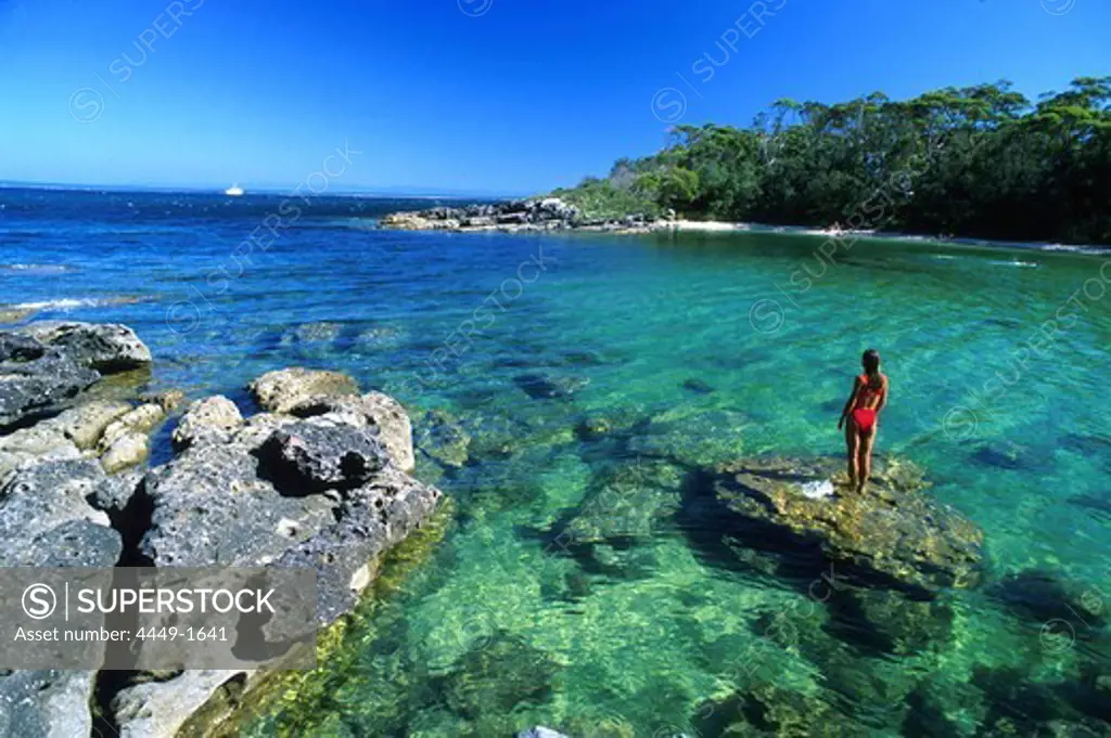 A woman standing on a rock at a bay under blue sky, Honeymoon Bay, Jervis Bay Marine Park, New South Wales, Australia