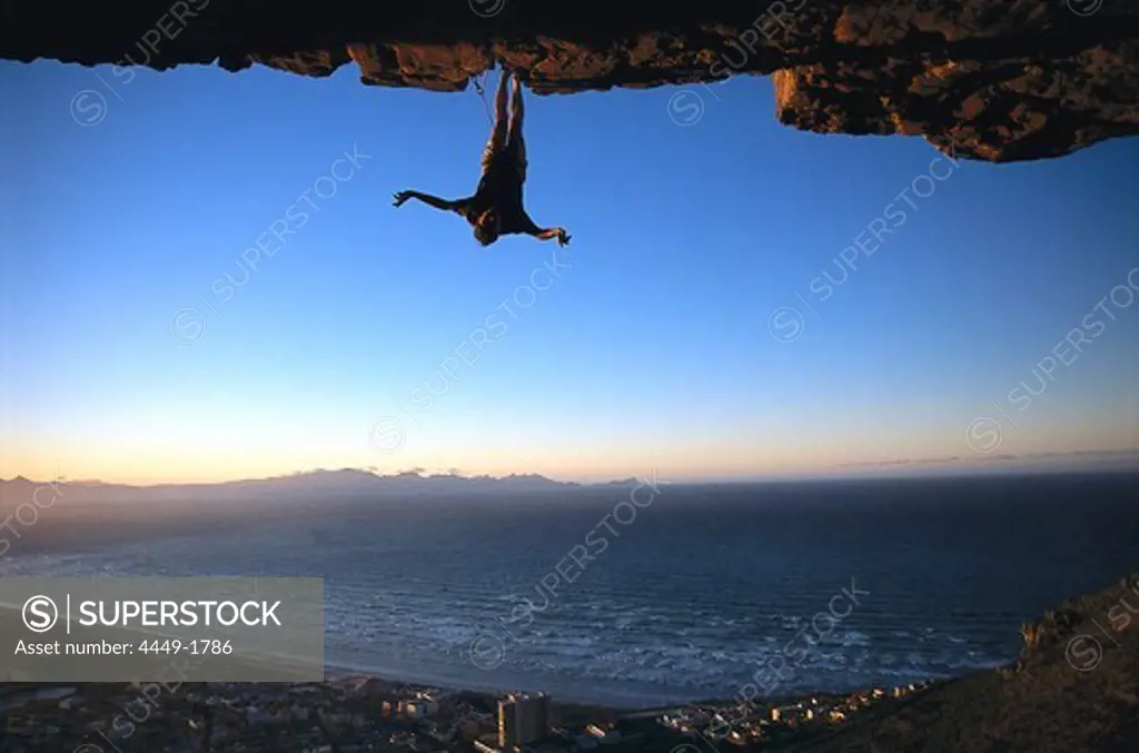 Rock climber hanging upside down, Muizenberg Bay, South Africa