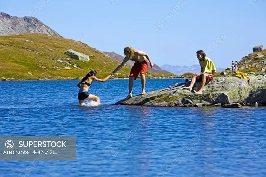 A young woman and two young men bathing, swimming in a mountain lake, cotton gras in the foreground, Laghi della Valletta, Gotthard Region, canton of Tessin, Ticino, Switzerland