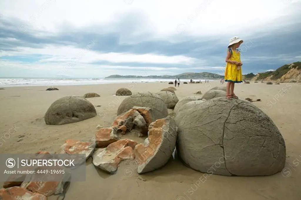 Girl standing on stone boulders, beach at the Moeraki Boulders, south of Oamaru, Eastcoast, South Island, New Zealand