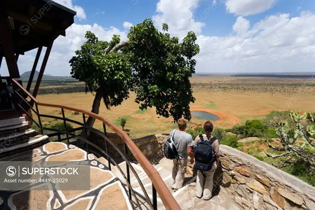 Guests looking over waterhole to savannah, Voi Safari Lodge, Tsavo East National Park, Coast, Kenya