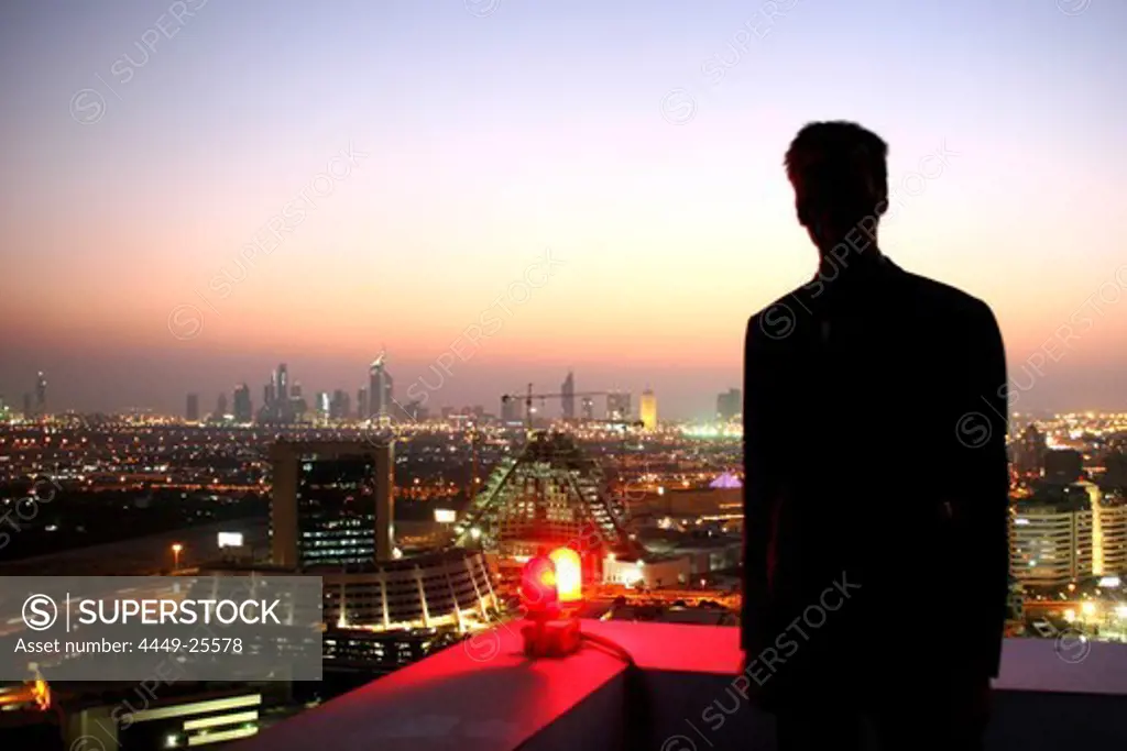 Man watching Dubai at dusk from roof of Grand Hyatt hotel, Dubai, United Arab Emirates, UAE