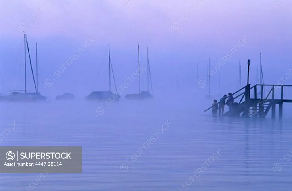 Europe, Germany, Bavaria, near Riederau, Lake Ammer, Sailing boats and people on the gangplank in the haze