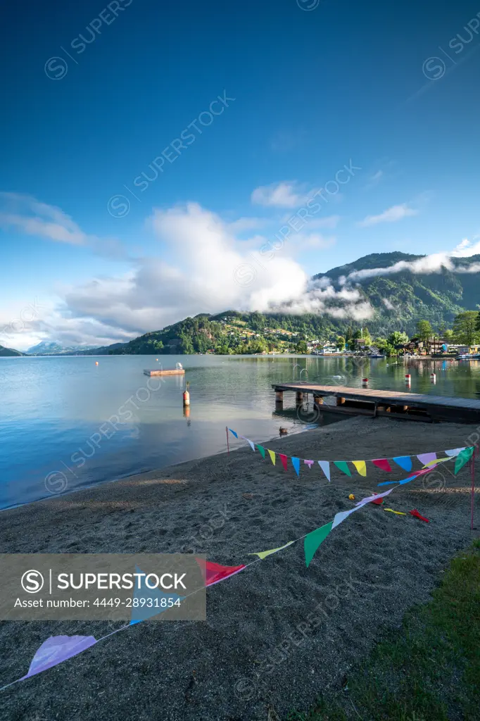 View over Lake Millstatt from the beach on the east bank of the alpine mountain and cultural landscape, Döbriach, Carinthia; Austria, Europe.