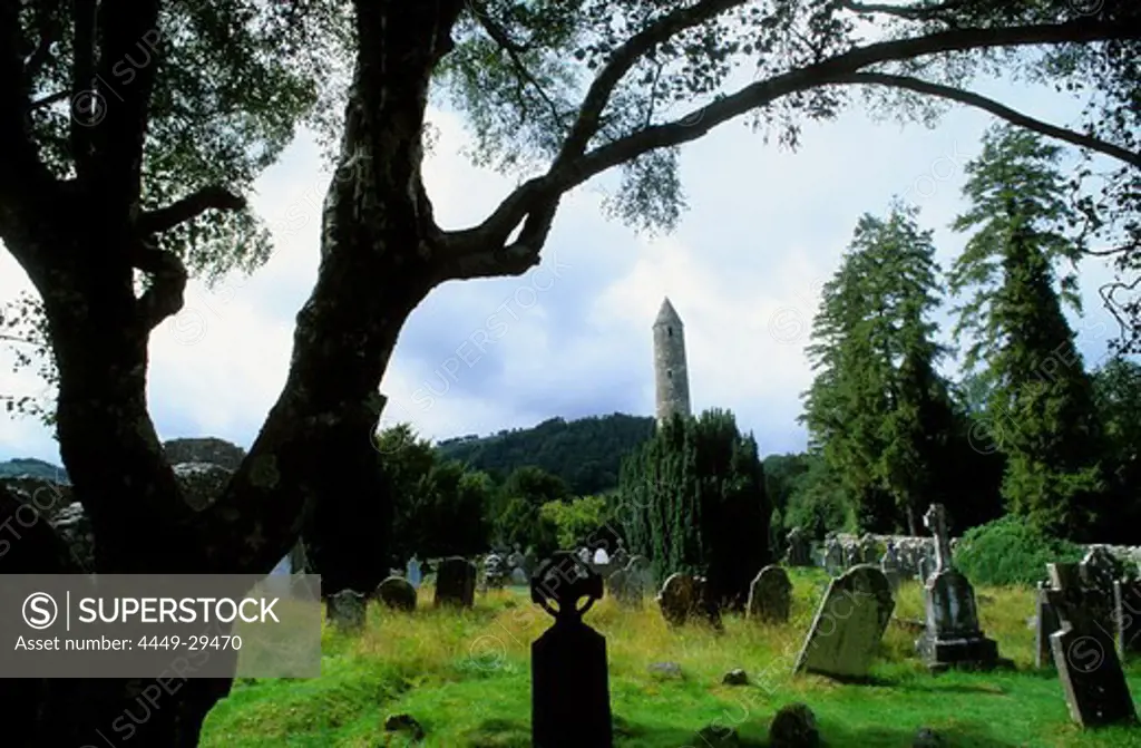 Round bastion and weathered graveyard under trees, Glendalough, County Wicklow, Ireland, Europe