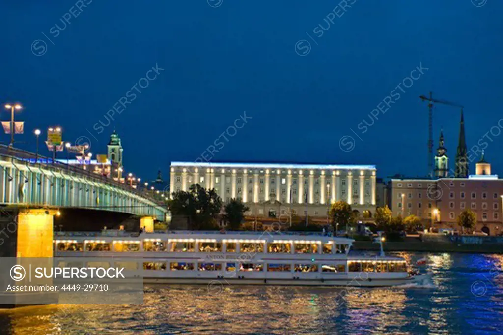 An excursion boat driving on the Danube at night, University of Art in the background, Linz, Upper Austria, Austria