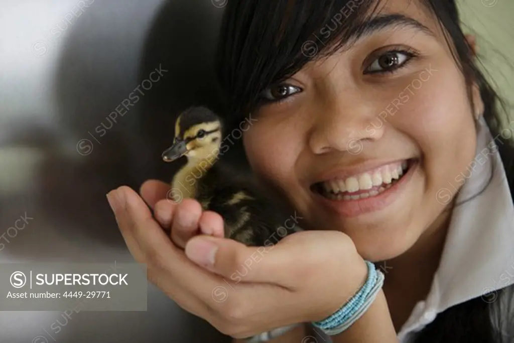 Young woman holding a duckling, smiling at camera, Germany