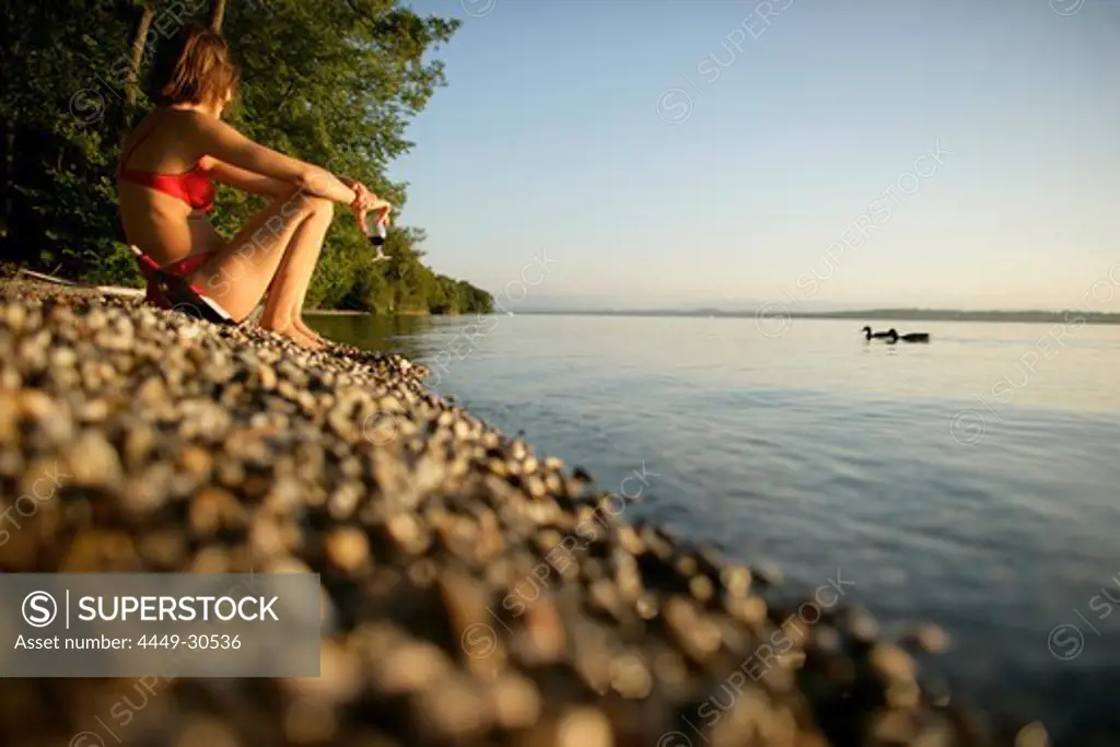 woman with glass of red wine sitting on the lake shore, Ammerland, Lake Starnberg, Bavaria, Germany