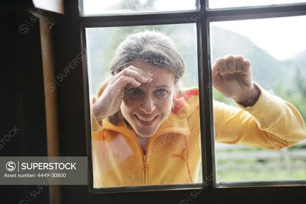 Woman looking through a window into alp lodge, Heiligenblut, Hohe Tauern National Park, Carinthia, Austria