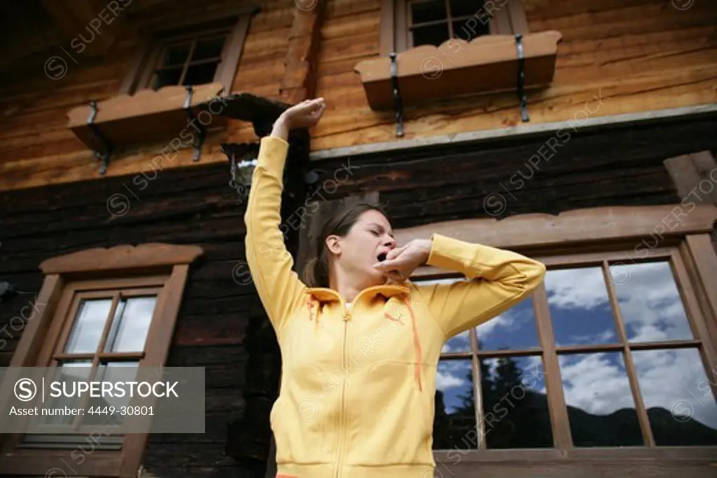 Woman yawning and stretching in front of alp lodge, Heiligenblut, Hohe Tauern National Park, Carinthia, Austria