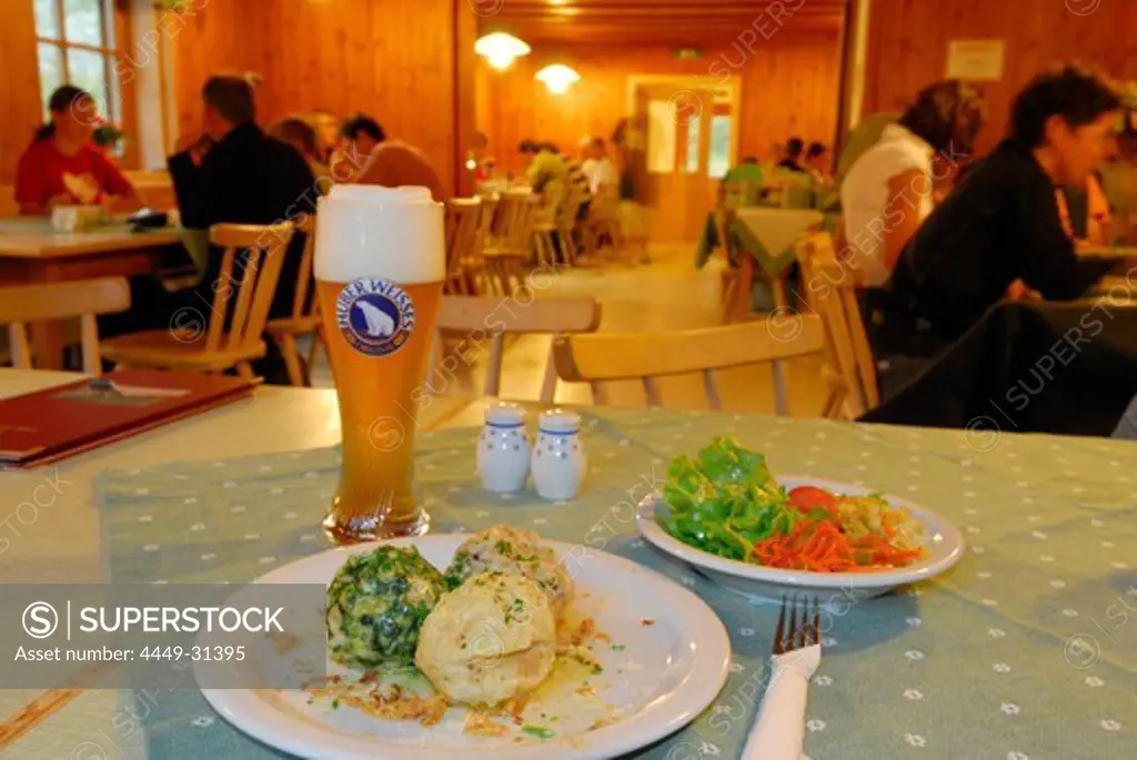 laid table with one portion of Tyrolean Knoedel, Spinatknoedel, Kasknoedel and Speckknoedel, mixed salad and weissbier, guests at tables out of focus in background, hut Franz-Senn-Huette, Stubaier Alpen range, Stubai, Tyrol, Austria