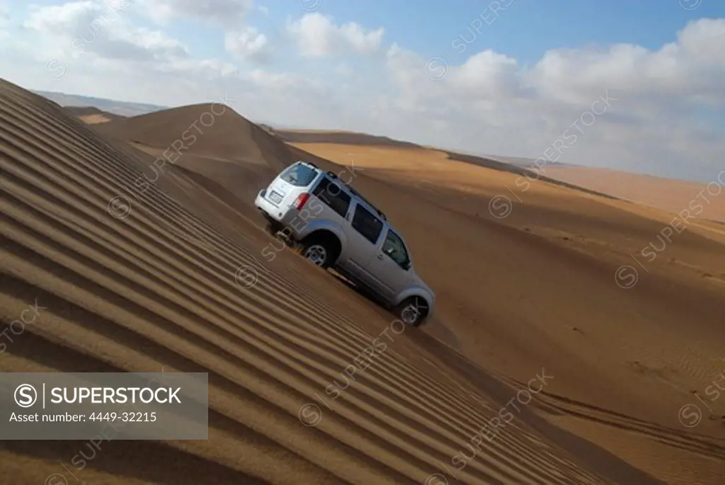 An all-terrain vehicle driving down a sand dune, Wahiba Sands, Oman, Asia