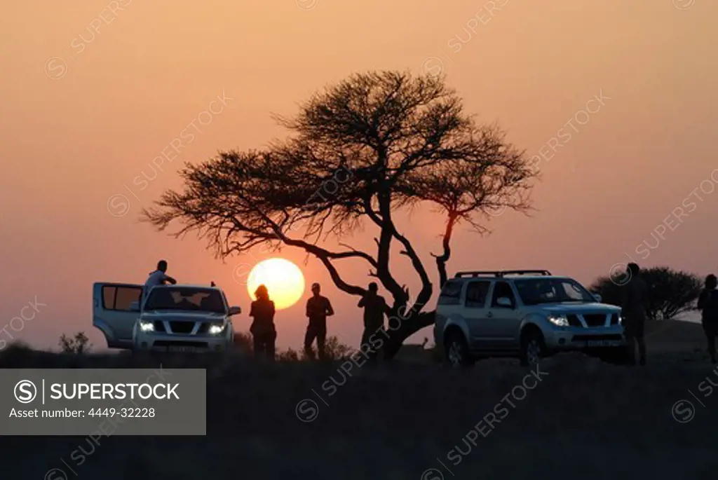 People and all-terrain vehicles in front of the setting sun, Al Hajar mountains, Oman, Asia